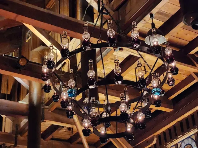 A round iron chandelier holding dozens of glass lamps, beneath a wooden beam ceiling