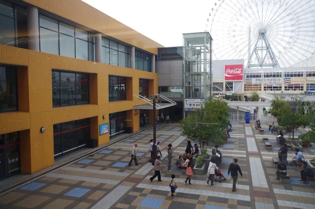 A paved plaza with a ferris wheel and crowds of visitors