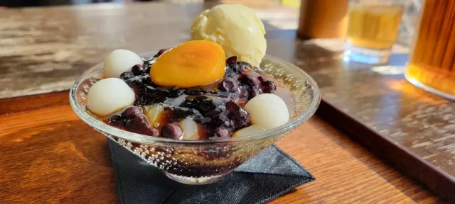 A small glass bowl with red beans, soft white balls, orange fruit and a scoop of ice cream