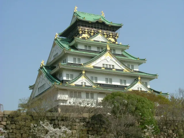 A white castle keep with green roofs and gold trim above a wall