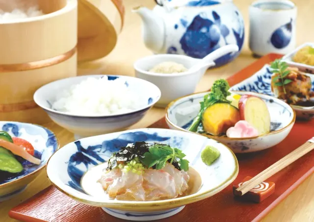 Blue and white dishes with slices of raw fish, white rice, a teapot and vegetable dishes