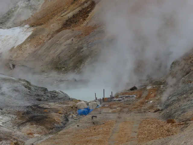 A bare brown and grey valley with steam rising from it