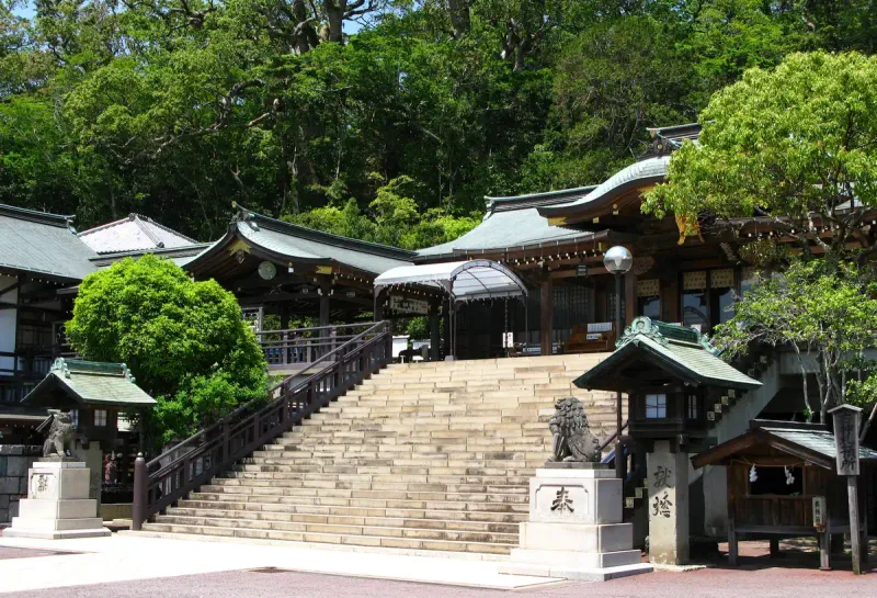 Shinto shrine buildings at the top of a stone stairway on a wooded slope