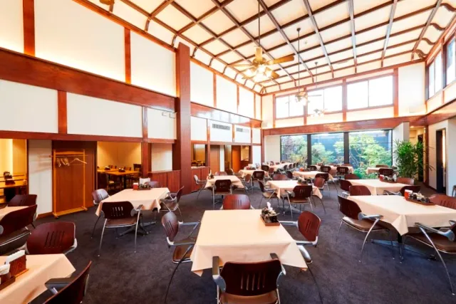 A bright hall with a glass ceiling, tables in white cloths and reddish wooden chairs