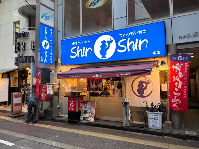 A frontage with a large blue sign, a pink awning and a long red banner beside the street