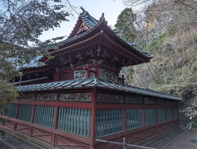 A red wooden temple building on a forested slope