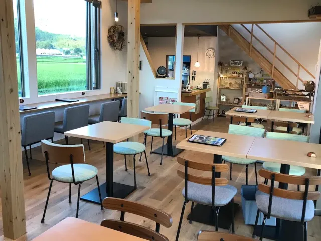 A bright room with tables, turquoise toned stools and a window facing a green field
