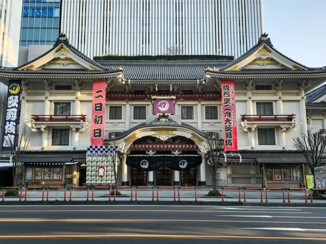 A traditional Japanese style theater facade with red banners, and a tall office tower behind it