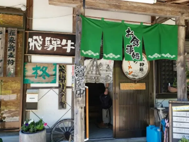 A wooden entrance with a green curtain, carved wooden signs and a round board with a drawing of a village house