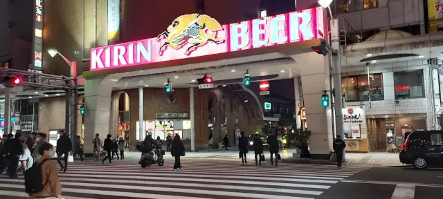 A pedestrian crossing at night facing the entrance of a covered arcade with a large neon sign