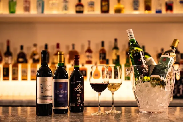 Three wine bottles, two glasses and an ice bucket on a counter facing bottle shelves