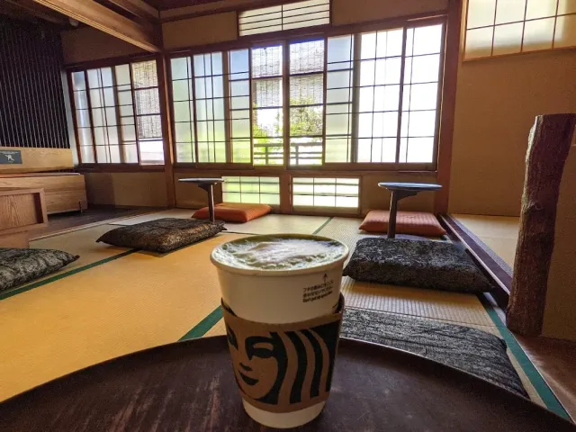 A paper cup with a hot drink on a table, with a matted room and paper windows behind it