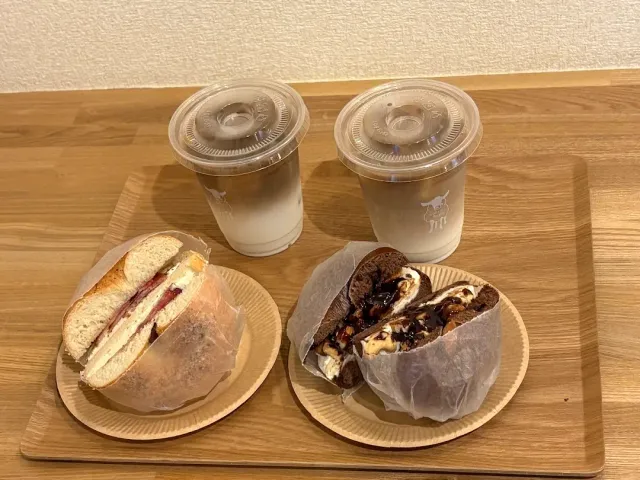 A wooden tray with two bun sandwiches and a pair of cold drink cups with lids