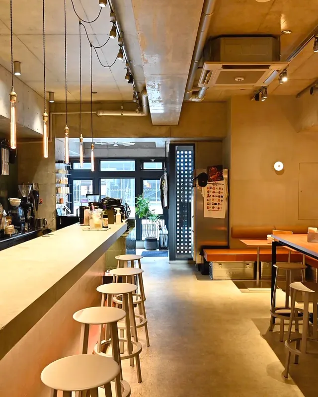 A space with a long counter, pale stools, hanging bulbs and a bare concrete ceiling