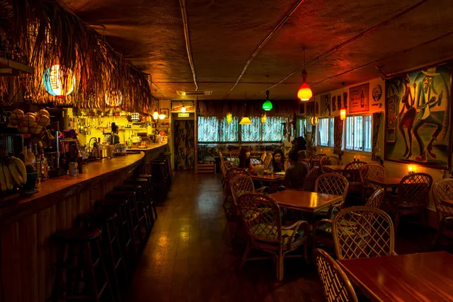 A hall with wicker chairs around wooden tables, a long counter and colourful hanging lamps