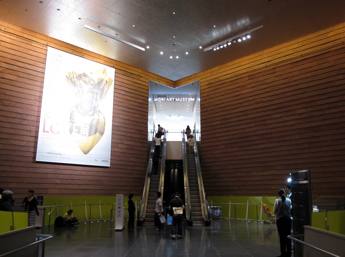 A wood clad entrance hall with escalators rising towards the lit museum sign