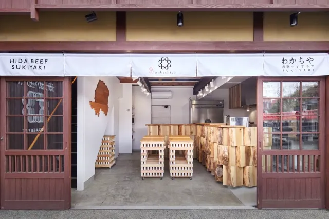 An open front with a white cloth curtain, light wooden stools and a counter built of logs
