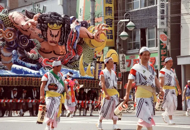 A colourful festival float and dancers in white costume in the street