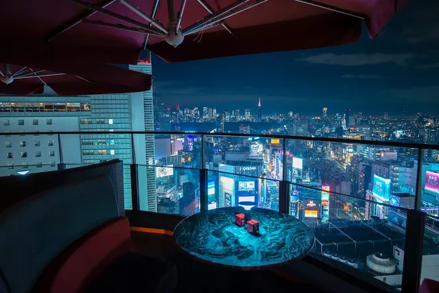 A table on a rooftop terrace under a parasol, facing the city lights at night