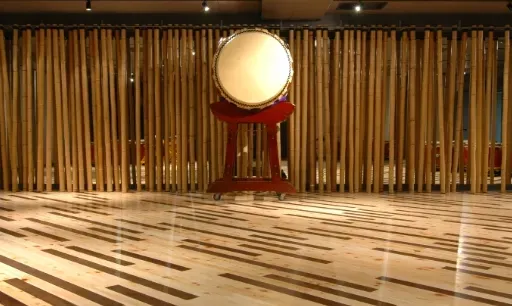 A large drum on a red stand in front of a bamboo wall, on a polished wooden floor