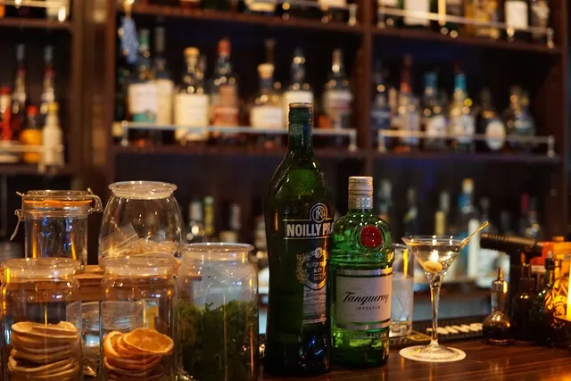 A martini glass on a counter beside jars of dried fruit, with shelves of bottles behind