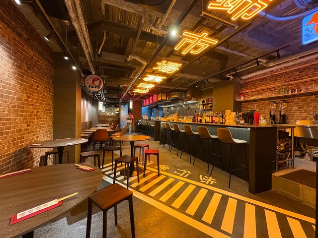 A hall with brick walls, a long bar and orange neon signs along the ceiling