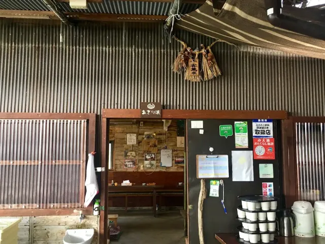 A corrugated metal structure with a wooden entrance, benches inside and straw bundles hanging from the ceiling