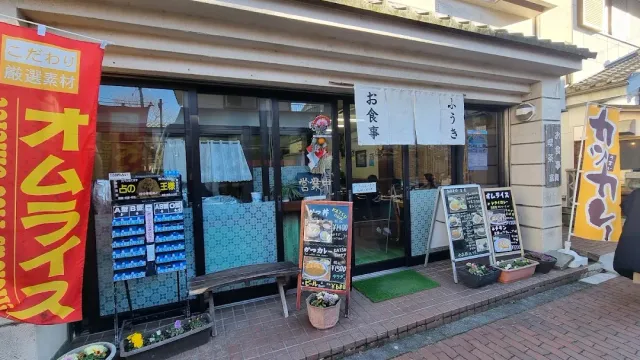 A frontage with street banners, photo menu boards, a display of food models and a wooden bench