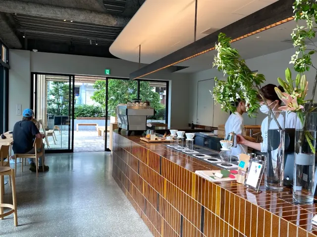 An orange tiled counter with baristas at work, green plants and a courtyard behind