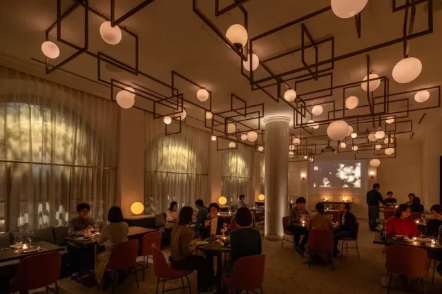 A large hall with globe lamps on hanging metal frames, diners and a white column
