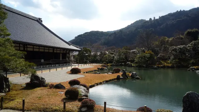 A long temple building across a garden pond, with forested hills behind