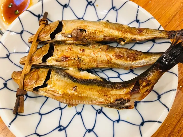Three grilled fish tied together on a plate with a blue net pattern