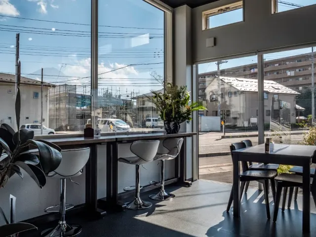 A bright space with full height windows, white stools at a counter facing the street and a black table