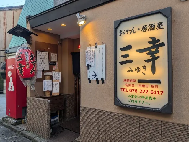 A street corner with a large lit sign in Japanese script, a big red lantern and a red machine