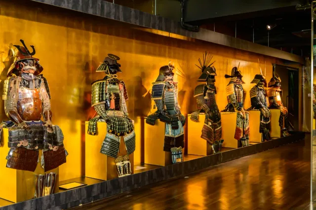 A row of armours on light pedestals against an orange wall, and a glossy wooden floor