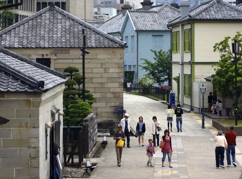 A paved street between restored historic buildings, with visitors and clipped trees