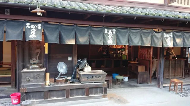 An old wooden house with dark cloth curtains, a charcoal stove and a metal kettle at the entrance