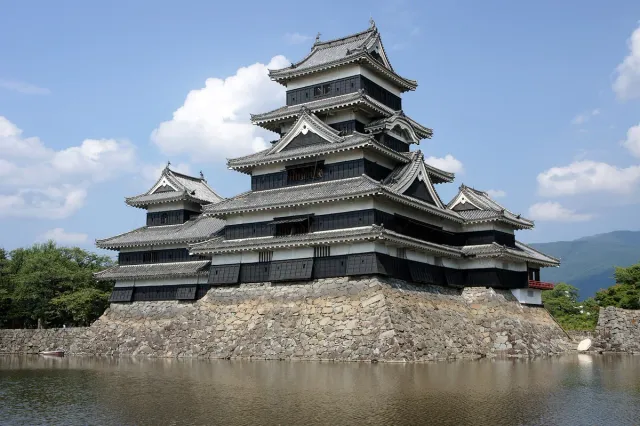 A black five-storey castle keep reflected in a moat