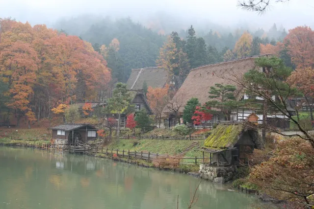 Thatched village houses around a lake, among autumn trees