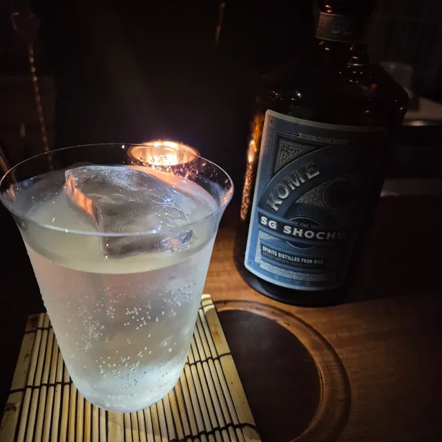 A glass of fizzy drink with an ice cube beside a bottle and a lit candle
