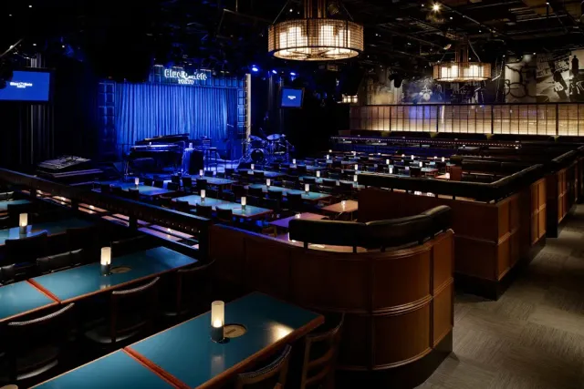 Tables in tiered rows in blue light facing a stage with a grand piano
