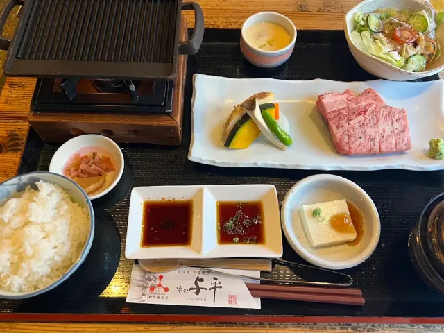 A meal tray with marbled beef slices, rice, sauces and a grill pan over coals