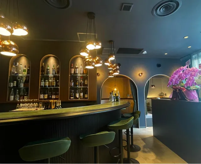 A curved bar with green stools, arched niches for bottles and hanging copper lamps