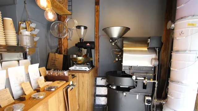 A large roasting machine beside a wooden counter with bags of beans and hanging bulbs