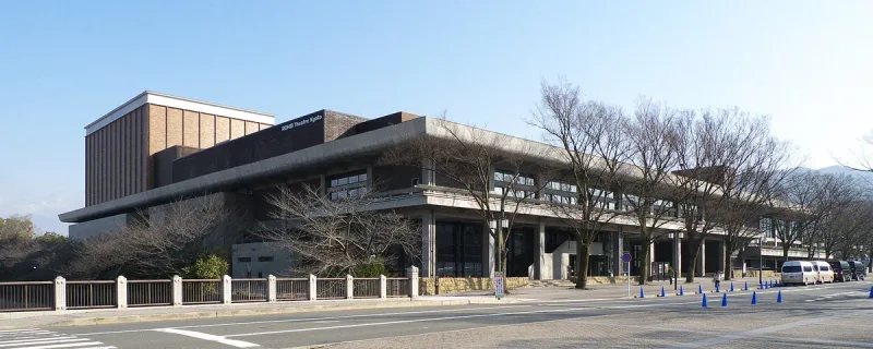 A modern concert hall building with straight lines, bare trees and a street in front