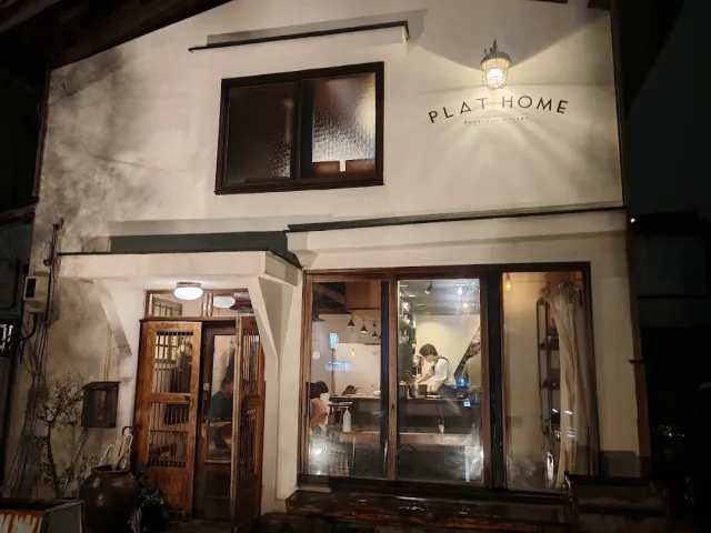 A white plastered building at night with a lit sign and a large window showing staff at work