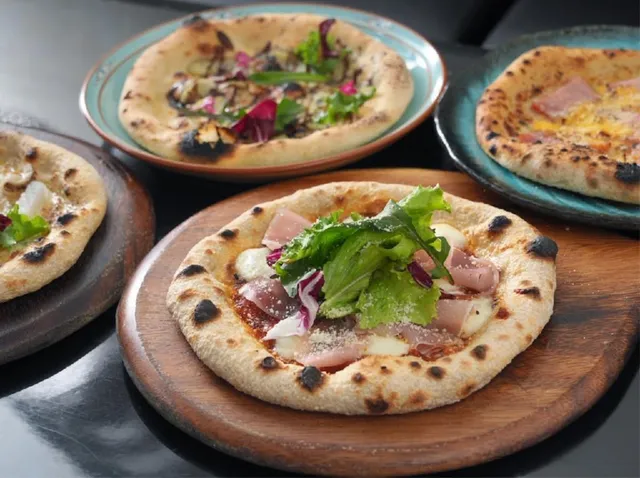 Thin pizzas with green leaves and cured ham on wooden boards and colourful plates