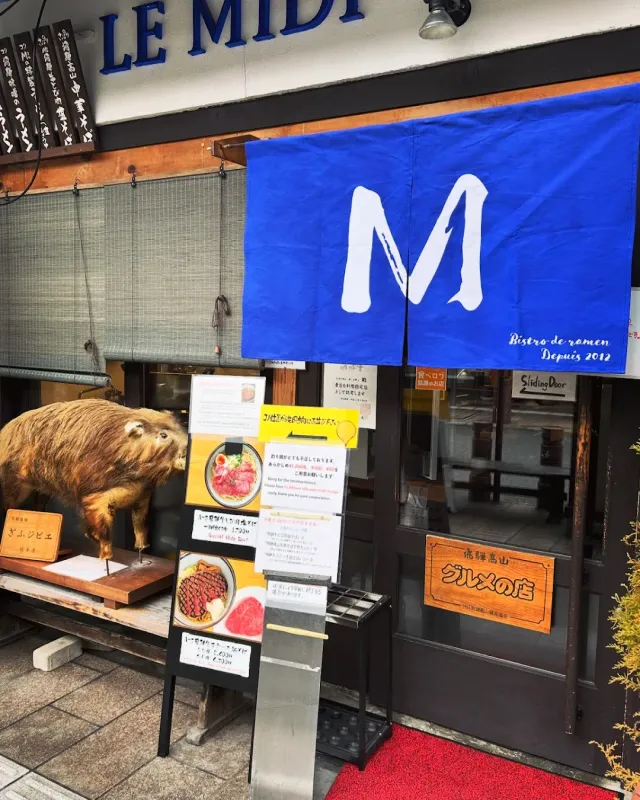 A frontage with a blue curtain and a large white letter, a stuffed wild boar and menu boards
