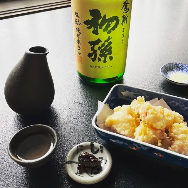 A bottle and a dark flask with a cup, and a fried dish in a blue and white vessel on a black table