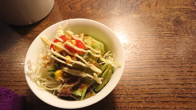 A small salad bowl with shredded cabbage, tomato and white dressing on a wooden table